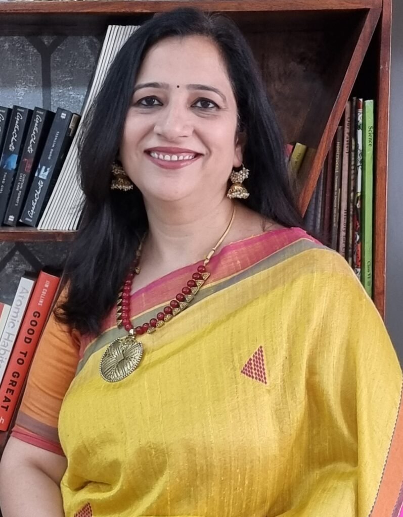 Vandana Bhasin in a yellow saree, in front of her bookshelf